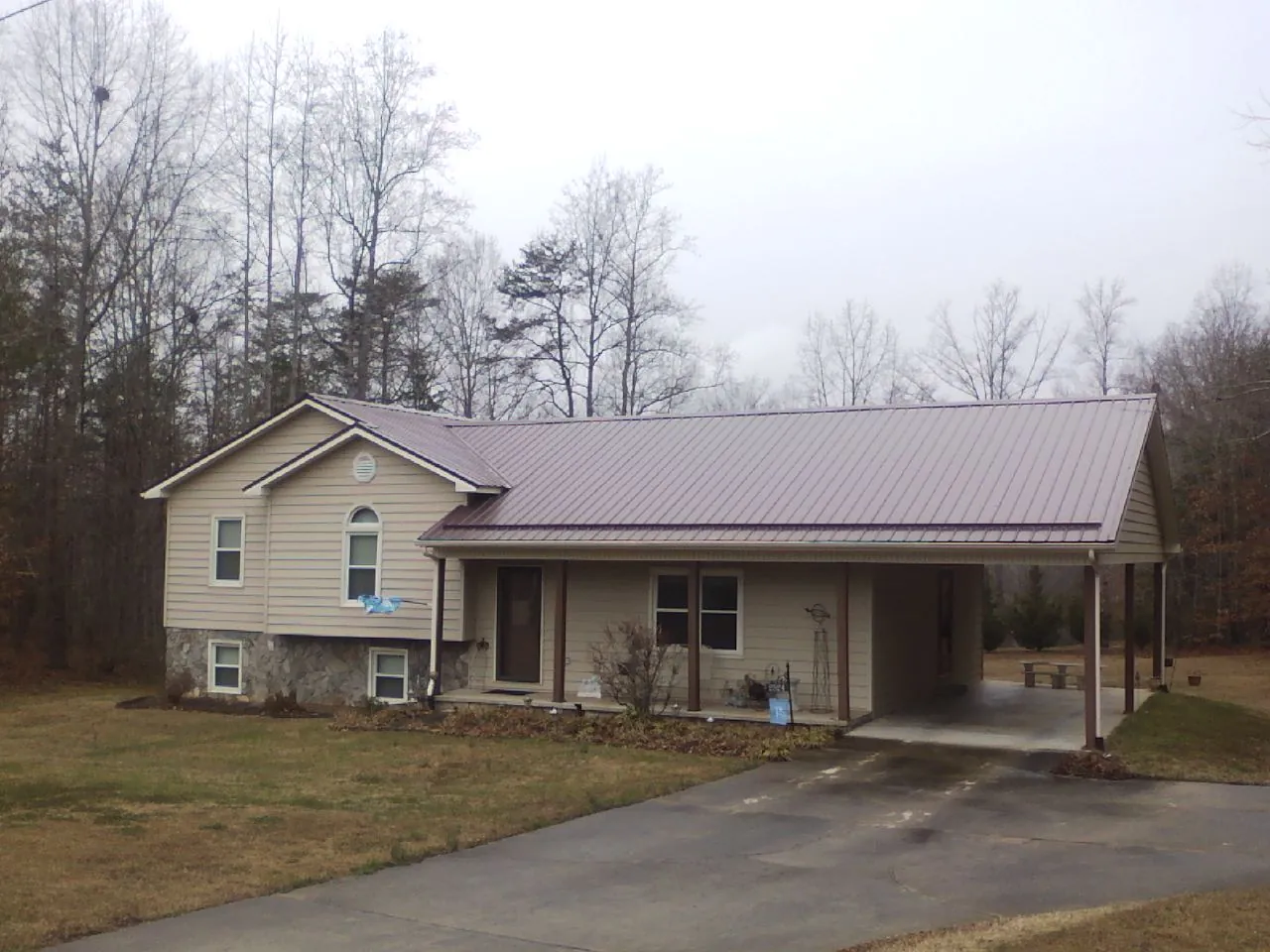 Burgundy metal roof on a tan split level home with an attached carport in Merino