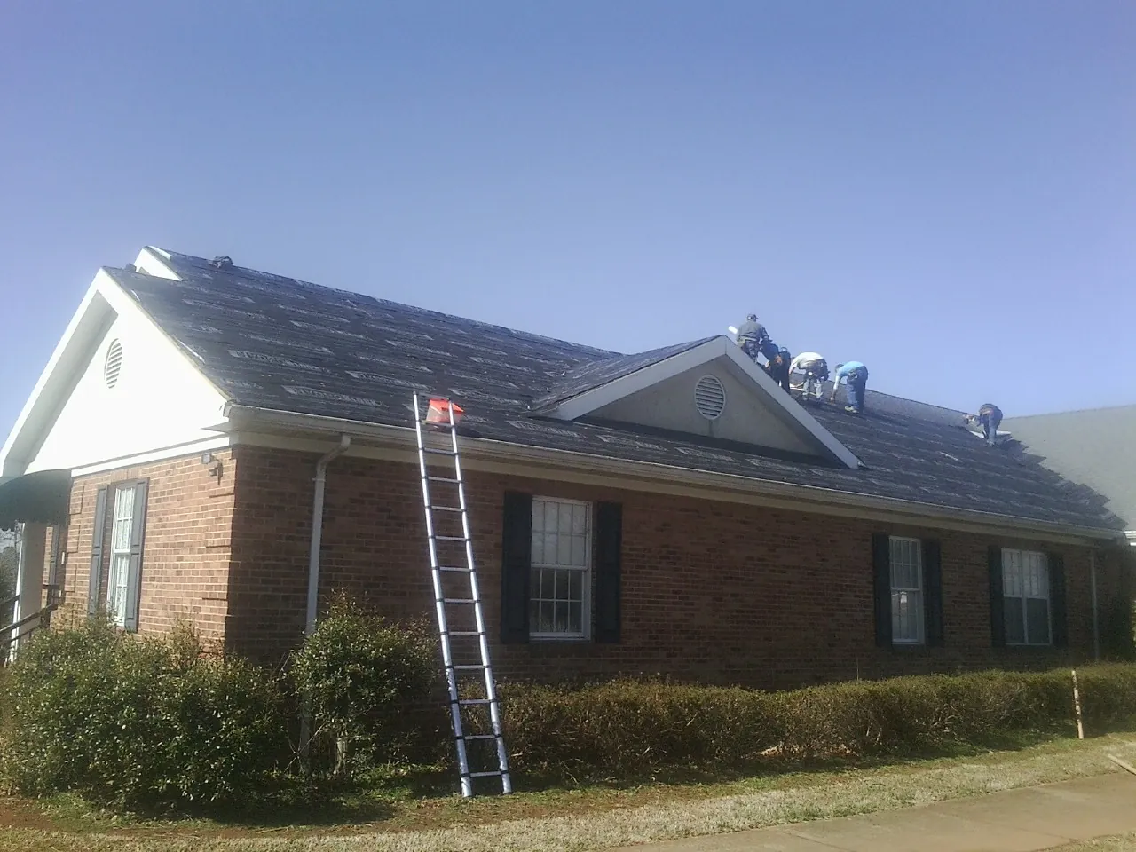 Crew tearing shingles off a brick ranch roof with a ladder set — Emergency Roof Repair work by our crew in Merino