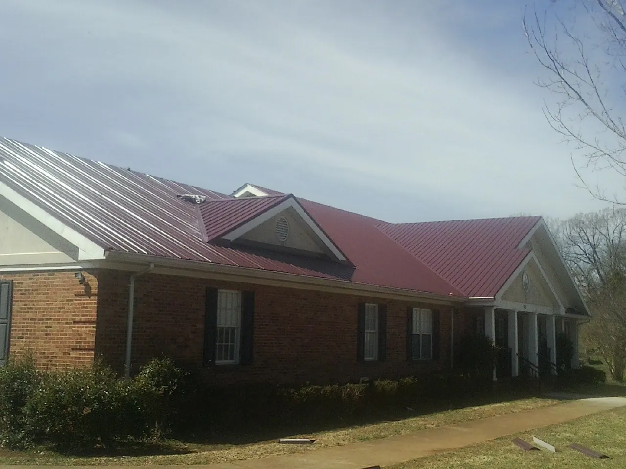 Red metal roof with gabled entries on a long brick building, from a Hail Damage Roof Repair job in Merino