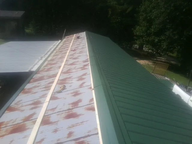 Old rusted panels beside newly installed green metal roofing — Wind Damage Roof Repair by Roofing Brothers in Merino