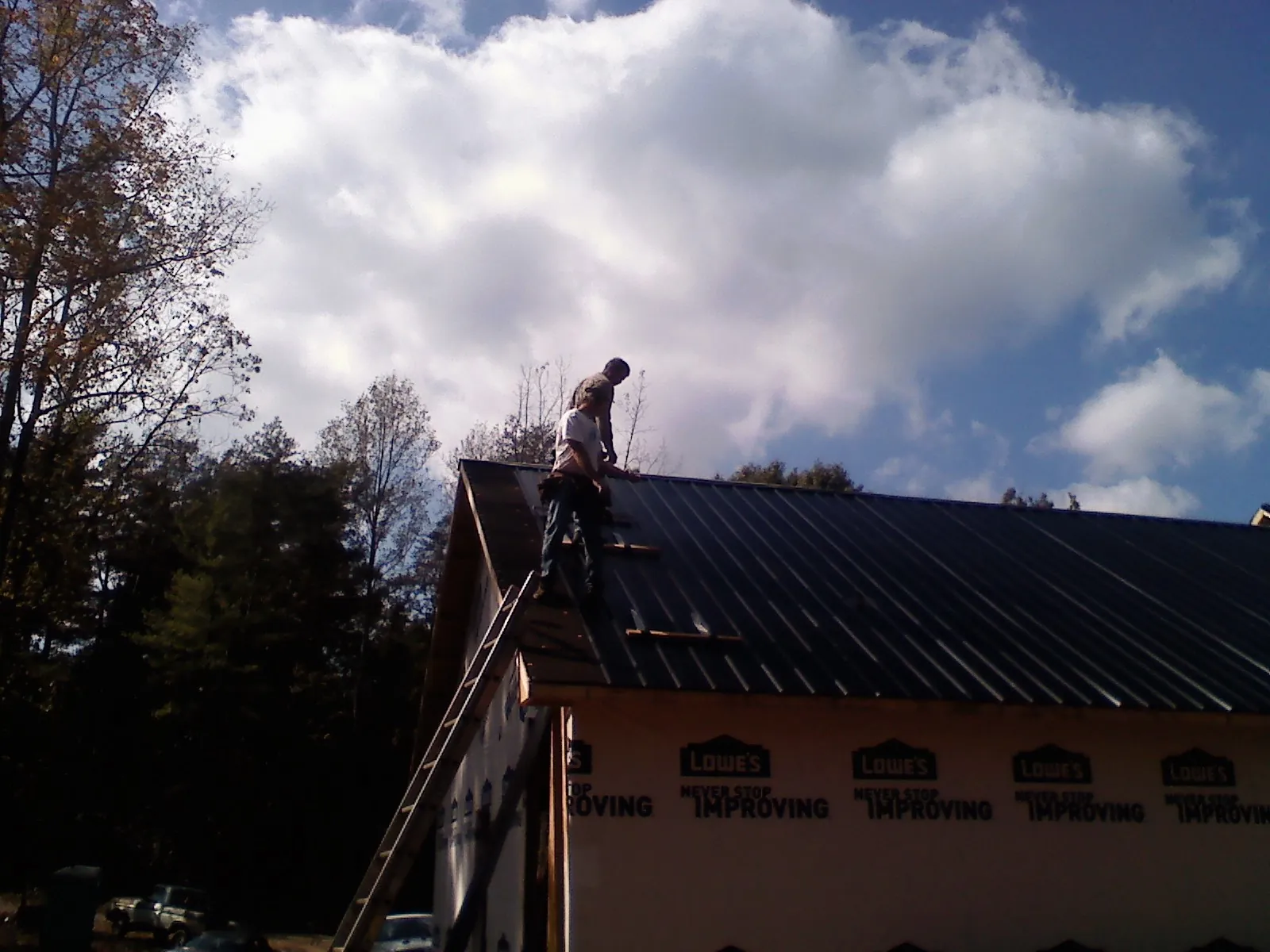 Roofer fastening dark metal panels high against a cloudy sky, from a Roof Inspection job in Merino