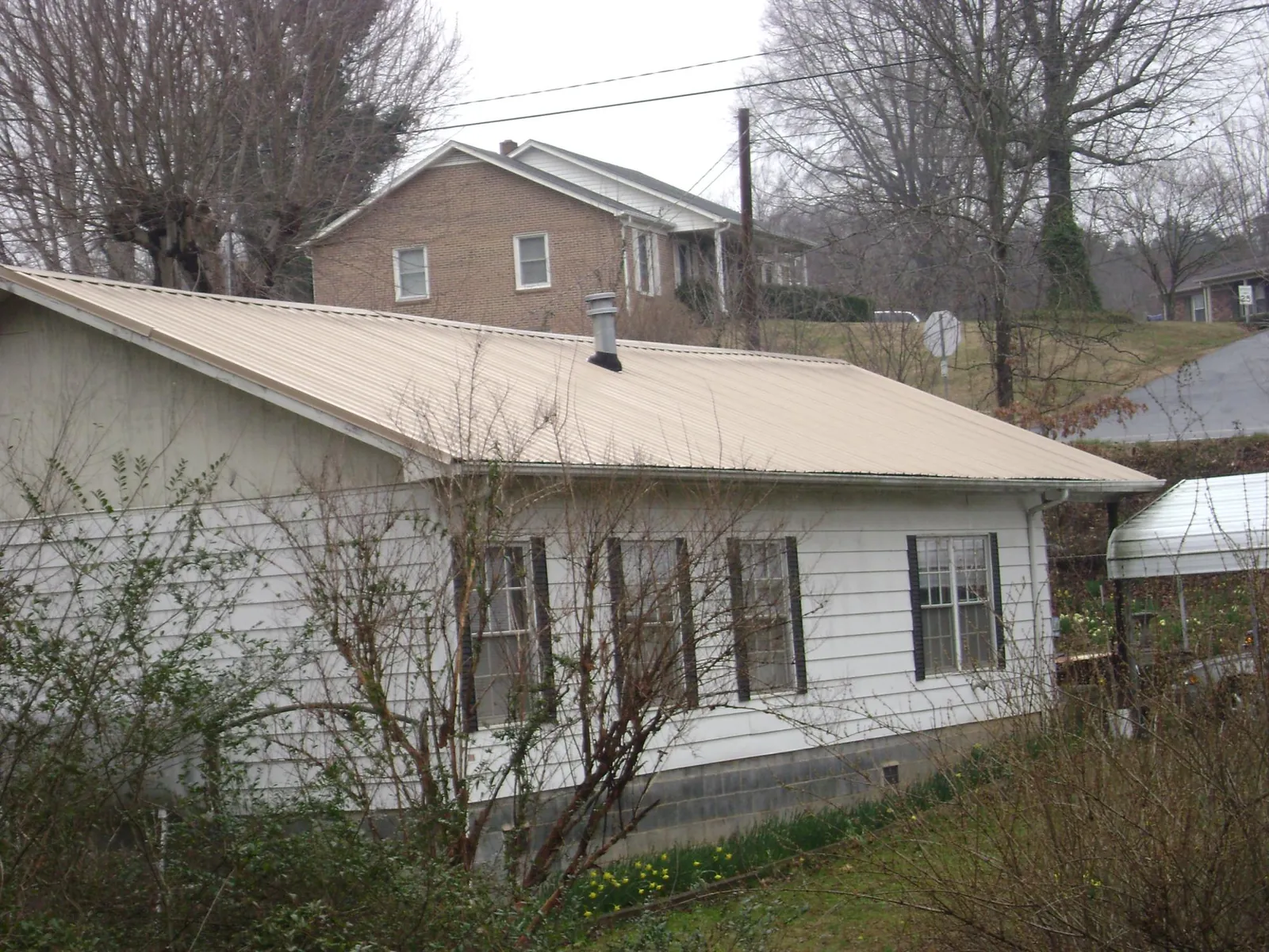 Tan metal roof on a white sided house set into a hillside — Commercial Roofing by Roofing Brothers in Merino