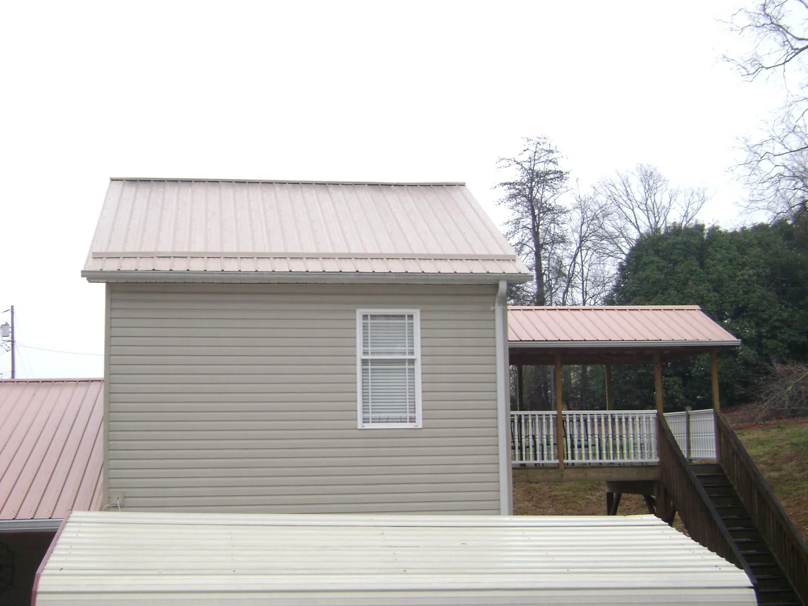 Tan metal roofs on a two story addition and attached porch, from a Roof Replacement job in Merino